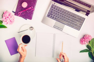 Çalışma alanı ile laptop, defter, gözlük, yazma el fincan kahve ve wisteria beyaz arka plan üzerinde çiçek kızın. Üstten Görünüm kadınsı ofis tablo Masası. Bağımsız çalışma yer.