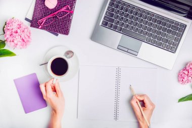 Çalışma alanı ile laptop, defter, gözlük, yazma el fincan kahve ve wisteria beyaz arka plan üzerinde çiçek kızın. Üstten Görünüm kadınsı ofis tablo Masası. Bağımsız çalışma yer.