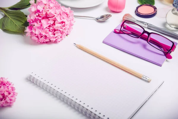 Vista superior Lugar de trabajo femenino con cuaderno para la planificación, accesorios cosméticos, cuaderno de bocetos, gafas y flores de glicina sobre el fondo blanco. Enfoque selectivo . —  Fotos de Stock