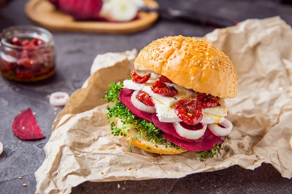 Vegitarian hamburger met bieten segmenten, microgreen spruiten, tofu kaas, gedroogde tomaten en UI op pakket kraftpapier op donkere stenen achtergrond met inhrediants. Zachte selectieve aandacht. Kopiëren van ruimte. — Stockfoto