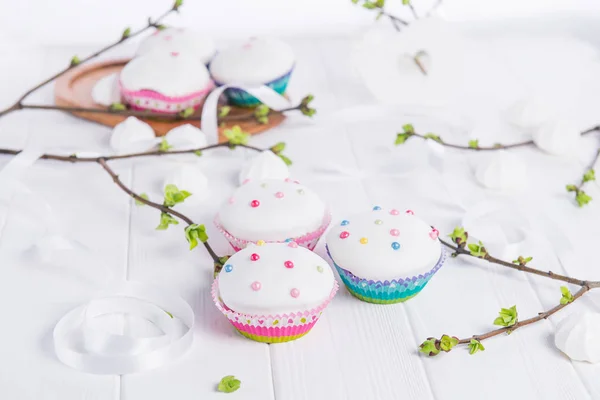 Oster-Cupcakes auf dem weißen Holztisch mit Zweigen mit jungen grünen Triebe, Satinband und leichten Merengue-Bonbons. Urlaubskonzept. Selektiver Fokus, Kopierraum. — Stockfoto