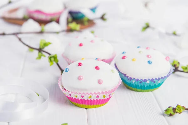 Oster-Cupcakes auf dem weißen Holztisch mit Zweigen mit jungen grünen Triebe, Satinband und leichten Merengue-Bonbons. Urlaubskonzept. Selektiver Fokus, Kopierraum. — Stockfoto