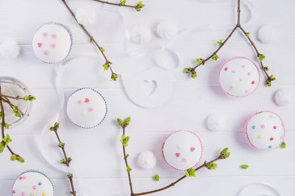 Oster-Urlaub Zusammensetzung von Zweigen mit jungen Triebe von Grün, dekorierte Cupcakes, Merengue-Bonbons, Band und farbige Vogelfigur auf Holzgrund. Kunstkonzept. Selektiver Fokus. — Stockfoto