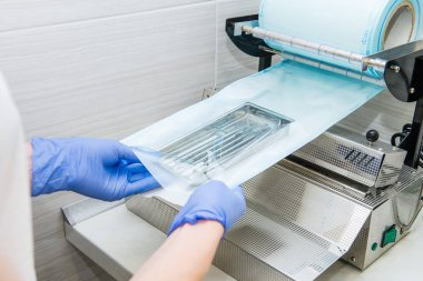 Dişçinin asistanı ellerinde eldiven diş araç kümesi ısıyla için vakum ambalaj makine kullanarak bir plastik torba içinde ambalaj kapatın. Kısırlık ve Emanet bakım kavramı. Seçici odak.