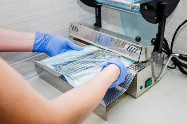Dişçinin asistanı ellerinde eldiven diş araç kümesi ısıyla için vakum ambalaj makine kullanarak bir plastik torba içinde ambalaj kapatın. Kısırlık ve Emanet bakım kavramı. Seçici odak.