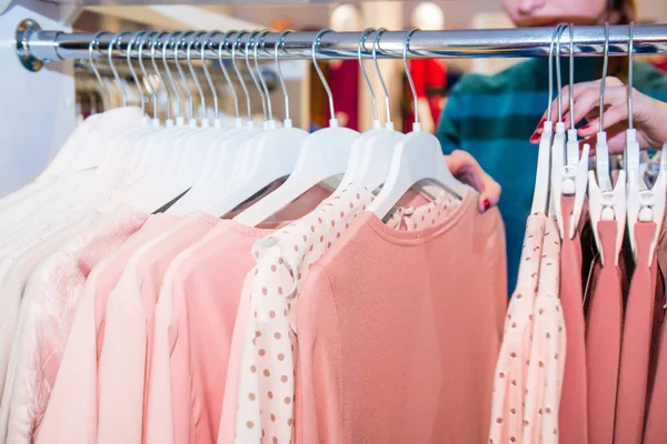 Cerca de manos femeninas buscando a través de perchas con ropa en la tienda, sala de exposición. Centro comercial. Comprador. Ventas. Centro Comercial. Enfoque selectivo . — Foto de Stock