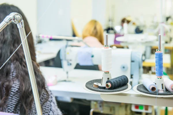 Bobines de fil dans l'équipement de couture avec des tailleurs de travail flous sur le fond. Le concept de la production de couture. Focus sélectif, espace pour le texte . — Photo