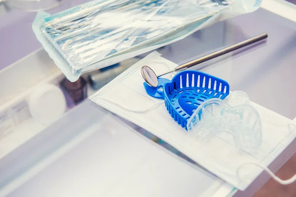 Conjunto de herramientas de equipo médico esterilizado empaquetado, espejo del dentista y moldes de mandíbula en la máscara en la mesa de trabajo en la clínica de ortodoncia. Enfoque selectivo, espacio para texto . —  Fotos de Stock