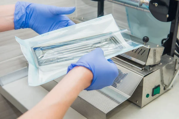 Fermer les mains de l'assistant du dentiste dans des gants emballant un ensemble d'instruments dentaires pour l'autoclavage dans un sac en plastique à l'aide d'une machine d'emballage sous vide. Concept de stérilité et de sécurité. Concentration sélective . — Photo