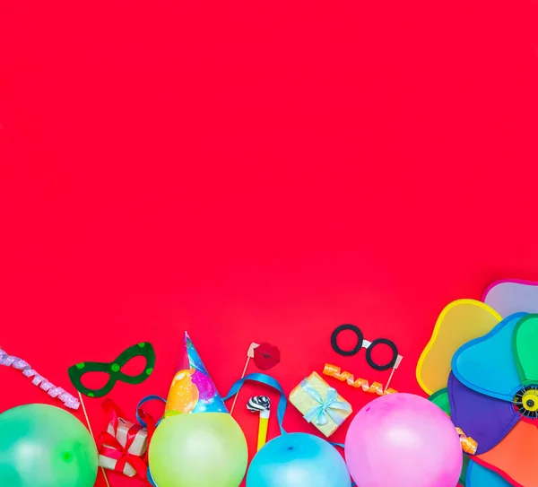 Rojo brillante Fondo festivo con herramientas de fiesta y decoración: globos, máscaras de carnaval divertidas, oropel festivo. Feliz cumpleaños tarjeta de felicitación. Concepto de diseño. Cuadrado. Seleccionar enfoque, lugar para texto . —  Fotos de Stock