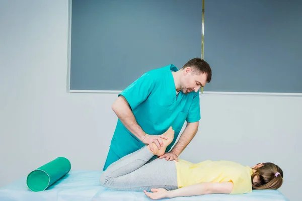 Jovem mulher recebendo massagem do terapeuta. Um quiroprático a esticar a perna do paciente no consultório médico. Exame físico neurológico. Osteopatia, quiropraxia, fisioterapia . — Fotografia de Stock