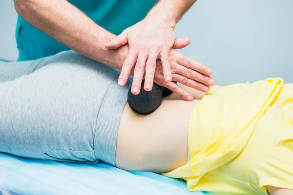 Mulher na fisioterapia recebendo massagem de bola do terapeuta. Um quiroprático trata a coluna vertebral dos lombos do paciente em consultório médico. Neurologia, osteopatia, quiropraxia. Foco seletivo, Fechar . — Fotografia de Stock