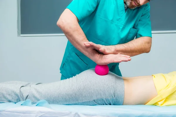 Kvinna på den sjukgymnastik som tar emot bollen massage från terapeuten. En kiropraktor behandlar patientens lårben skinkan i medicinsk kontor. Neurologi, osteopati, kiropraktik. Selektiv fokus, närbild. — Stockfoto