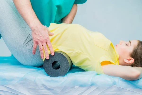 Mulher na fisioterapia fazendo exercícios físicos com seu terapeuta, eles usam um rolo de massagem. Um quiroprático trata a coluna vertebral dos lombos do paciente em consultório médico. Neurologia, Osteopatia, quiropraxia . — Fotografia de Stock