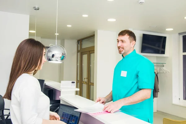 Mannelijke arts praten en werken shedule bespreken met jonge vriendelijke vrouwelijke receptioniste bij de receptie van het ziekenhuis. Bezetting, personeel interactie concept. Selectieve aandacht, ruimte voor tekst. — Stockfoto