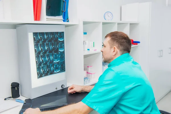 Médico varón mirando la imagen de rayos X de la columna cervical en su consultorio. Osteopatía, quiropráctica, fisioterapia. Salud, roentgen, personas y concepto de medicina. Enfoque selectivo, espacio para texto . — Foto de Stock