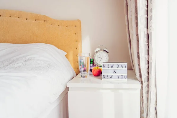 Inspiration Motivational Life Quotes New day New you message on lightened box with alarm clock, rubik's cube, notebooks on the bedside table near bed in the sunlight. Good morning mood. Copy space. — Stock Photo, Image