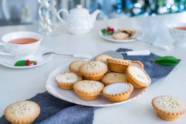 Traditional english festive pastry mince pies on served for tea time table with lightened christmas tree on background. Cozy home mood. Close up, selective focus. Copy space. — Stock Photo, Image