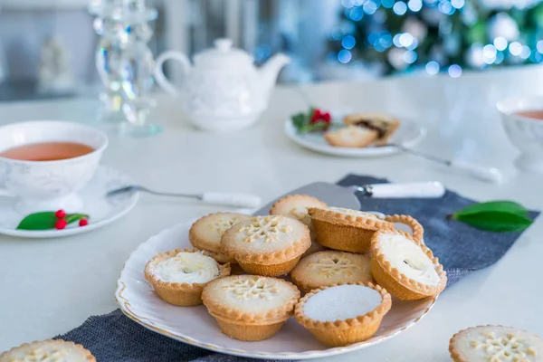 Traditional english festive pastry mince pies on served for tea time table with lightened christmas tree on background. Cozy home mood. Close up, selective focus. Copy space. — Stock Photo, Image