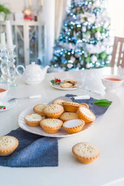 Traditional english festive pastry mince pies on served for tea time table with lightened christmas tree on background. Cozy home mood. Vertical card. Close up, selective focus. Copy space. — Stock Photo, Image