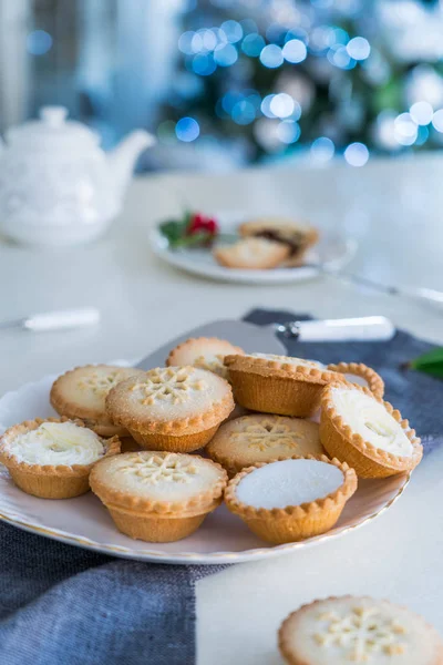 Traditional english festive pastry mince pies on served for tea time table with lightened christmas tree on background. Cozy home mood. Vertical card. Close up, selective focus. Copy space. — Stock Photo, Image