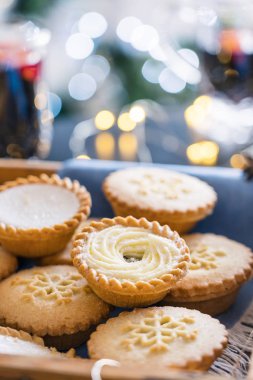 Sıcak kompozisyonu geleneksel İngiliz şenlikli pasta kıymalı turtalar ahşap tepside ve arka planda sıcak şarap içecekleri, ışık çelenkleri ve yılbaşı ağacı bulanık arka planda. Dikey. Kapat.