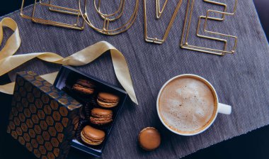 En üstteki kahve fincanı, kurabiye kutusu ve gri peçetede aşk kelimesi. Sevgililer için sıcak bir kahvaltı. Siyah İskandinav tarzında romantik bir sabah. Hygge Sevgililer Günü konsepti. Afiş geniş. Boşluğu kopyala