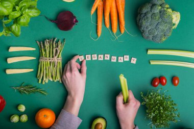 Üst düzey erkek eller yeşil arka planda taze çiğ sebzeler ve meyvelerle Veganayı gözler önüne seriyor. Vejetaryen ve vejetaryen diyeti. Vejetaryenlik. Sürdürülebilir yaşam tarzı, bitkisel gıdalar
