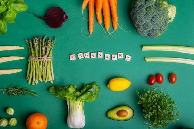 Yeşil arka planda sağIıklı çiğ sebzeler ve ahşap bloklarda Veganay mesajı. Vejetaryen ve vejetaryen diyeti. Vejetaryenlik kavramı. Sürdürülebilir yaşam tarzı, iyi, gerçek bitkisel gıdalar.
