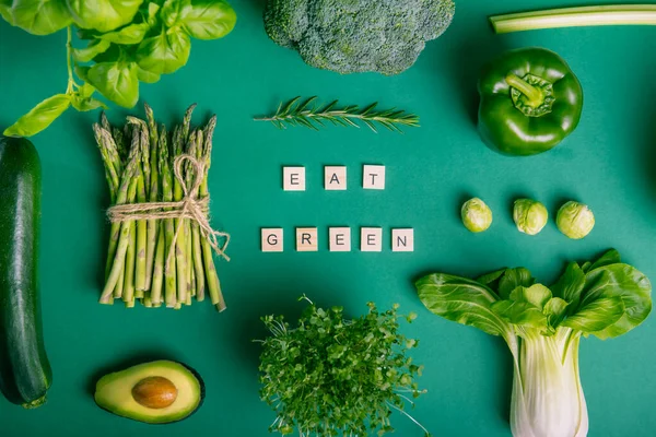 木のブロックに緑のメッセージを食べと緑の背景に健康的な生野菜のトップビューセット ベジタリアン ビーガン対応 菜食主義の概念 持続可能なライフスタイル 本物の植物性食品 — ストック写真