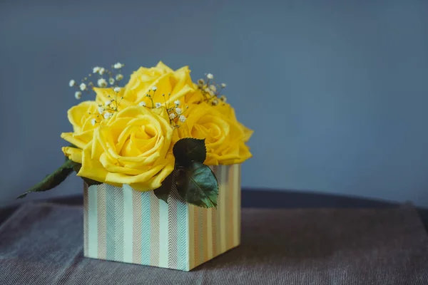 Yellow roses bouquet with green leaves in box on grey background. Woman or mother day gift idea. Festive background with copy space