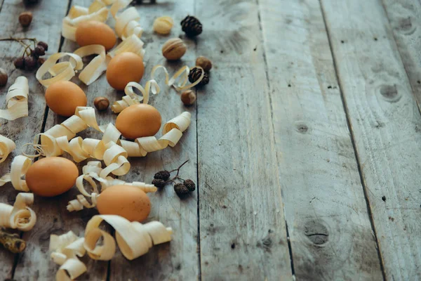 Raw natural gold eggs with nature details, nuts, cones and wood shavings on an old vintage wooden table. The rural or rustic kitchen still life. Eco Easter concept. Copy space.