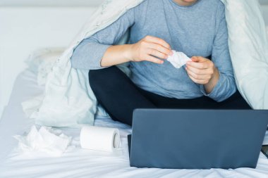 Sıcak bir battaniyenin altında yatıp dizüstü bilgisayarla çalışan ve burnunu sildikten sonra elinde peçete tutan beyaz bir adam yok. Hastalık sırasında evde çalışmak. Boşluğu kopyala, Seçici odak