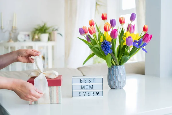 女性の手が花瓶や言葉でライトボックスにカラフルな春の花花束と大理石のテーブルの上にギフトボックスを開いています最高のお母さんこれまで 軽めの室内 幸せな母の日の背景 スペースのコピー — ストック写真