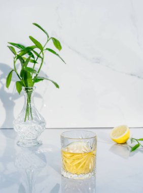 Sarı kokteylli kristal bardak, taze yeşillikli vazo ve mermer zemin üzerinde yarım limon. Yeşil çay ve alkol dolu bir kadeh. Doğrudan güneş ışığı ve gölgeler. Minimalizm. Boşluğu kopyala.