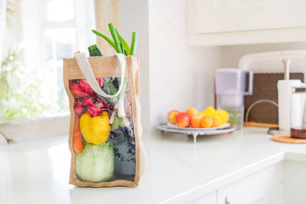 Fresh organic vegetables delivery concept. Reusable bio eco sackcloth fabric bag packaging on marble white kitchen table. Local farmer healthy food. Zero waste and plastic-free lifestyle. Copy space