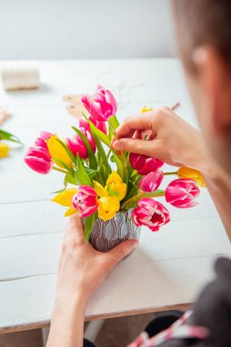 Lale kullanarak bahar buketi yapan genç adam yok. Çiçekçiliğin internetten öğrenimi. Çiçek düzenlemeyi öğreniyorum. Çiçek teslimatı. Erkek çiçekçi düzen yaratıyor. Seçici odaklanma. Dikey kart.