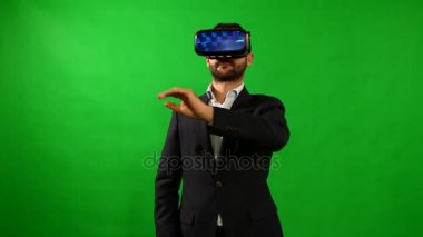 Takım elbiseli adam sanal gerçeklik gözlük kullanır. VR. yeşil arka plan. Bir adam sanal arabirimi kullanır. Yüksek teknoloji ürünü cihazlar. Yeşil bir arka plan üzerinde el hareketi. Sanal gerçeklik kask. 4 k çözünürlük.