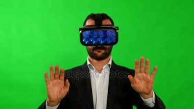 Takım elbiseli adam sanal gerçeklik gözlük kullanır. VR. yeşil arka plan. Bir adam sanal arabirimi kullanır. Yüksek teknoloji ürünü cihazlar. Yeşil bir arka plan üzerinde el hareketi. Sanal gerçeklik kask. 4 k çözünürlük.