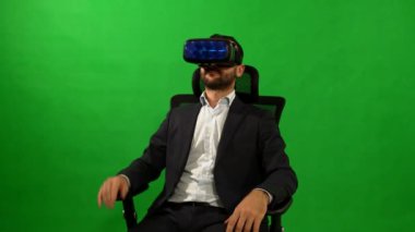 Takım elbiseli adam sanal gerçeklik gözlük kullanır. VR. yeşil arka plan. Bir adam sanal arabirimi kullanır. Yeşil bir arka plan bir koltukta oturan işadamı. Sanal gerçeklik kask. 4 k çözünürlüklü. Yüksek teknoloji.