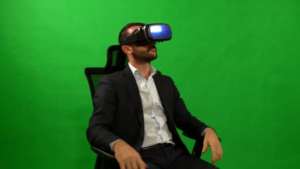 Homme en costume utilise des lunettes de réalité virtuelle. Fond de VR. Green. Un homme utilise interface virtuelle. Homme d’affaires assis dans un fauteuil sur un fond vert. Casque de réalité virtuelle. résolution de 4 k. Hi-tech. — Video