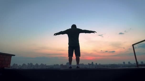 The guy jumps from the edge of the roof, spreading his arms to the side. Beautiful sunset. — Stock Video