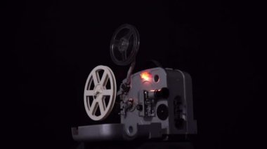 Retro film projektör siyah bir arka plan. Filmin 8 milimetre. Hareketli parçaları ve projektör ışığı yanıp sönüyor. Film hareket ediyor.