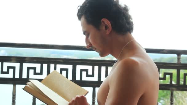 Mann liest Buch und entspannt auf Balkon — Stockvideo