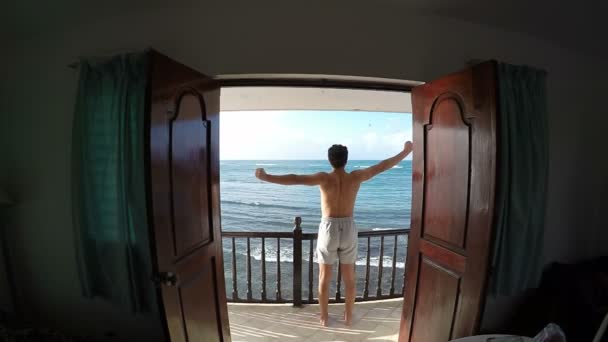 Людина розтягується на балконі з видом на море — стокове відео