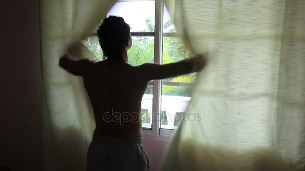 Mann öffnet Vorhänge und schaut nach draußen — Stockvideo