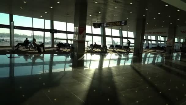 Aeropuerto terminal interior, personas viajeros pasajeros siluetas esperando en un salón, hall vista, hermoso fondo con sol, dolly shot desde escaleras mecánicas — Vídeo de stock
