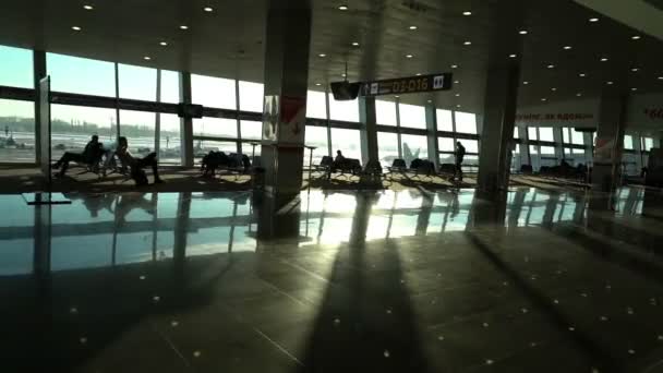 Airport terminal interior, people travellers passengers silhouettes waiting in a lounge, hall view, beautiful background with sunshine, dolly shot from escalator — Stock Video