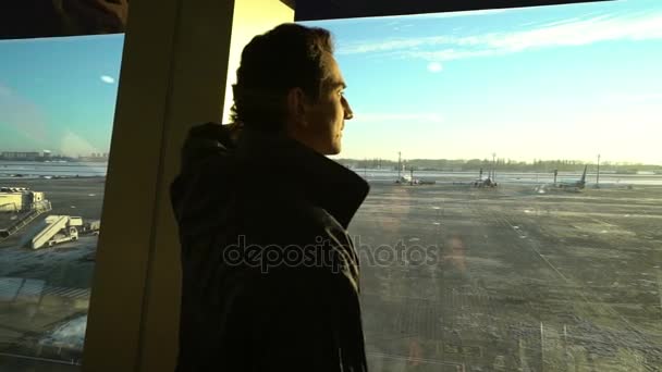 Homme debout à la fenêtre à l'intérieur du terminal de l'aéroport, personnes voyageurs silhouettes passagers attendant dans un salon, vue sur le hall, beau fond avec soleil, dolly shot de l'escalator, Voyage — Video