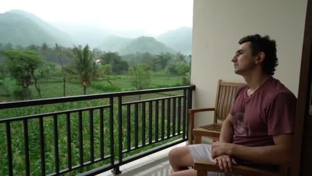 Traurig unglücklich deprimiert verwüstet, verwüstet, ruiniert Mann sitzt allein auf einem Balkon mit wunderbaren grünen Natur Hintergrundblick — Stockvideo